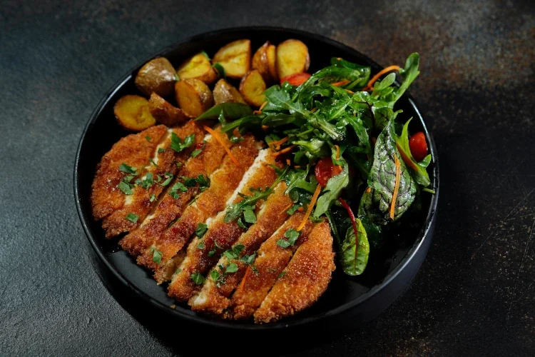 Pork schnitzel with garnish and potatoes in a black bowl