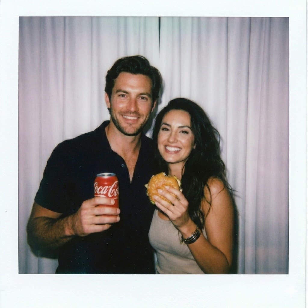 Take a photo taken with a Polaroid camera. The photo should look like an ordinary photograph, without an explicit subject or property. The photo should have a slight blur and a consistent light source, like a flash from a dark room, scattered throughout the photo. Don't change the face. Change the background behind those two people with white curtains. With that boy and me make a cute poses. Make the boy holding a red coca cola can and girl a burger.