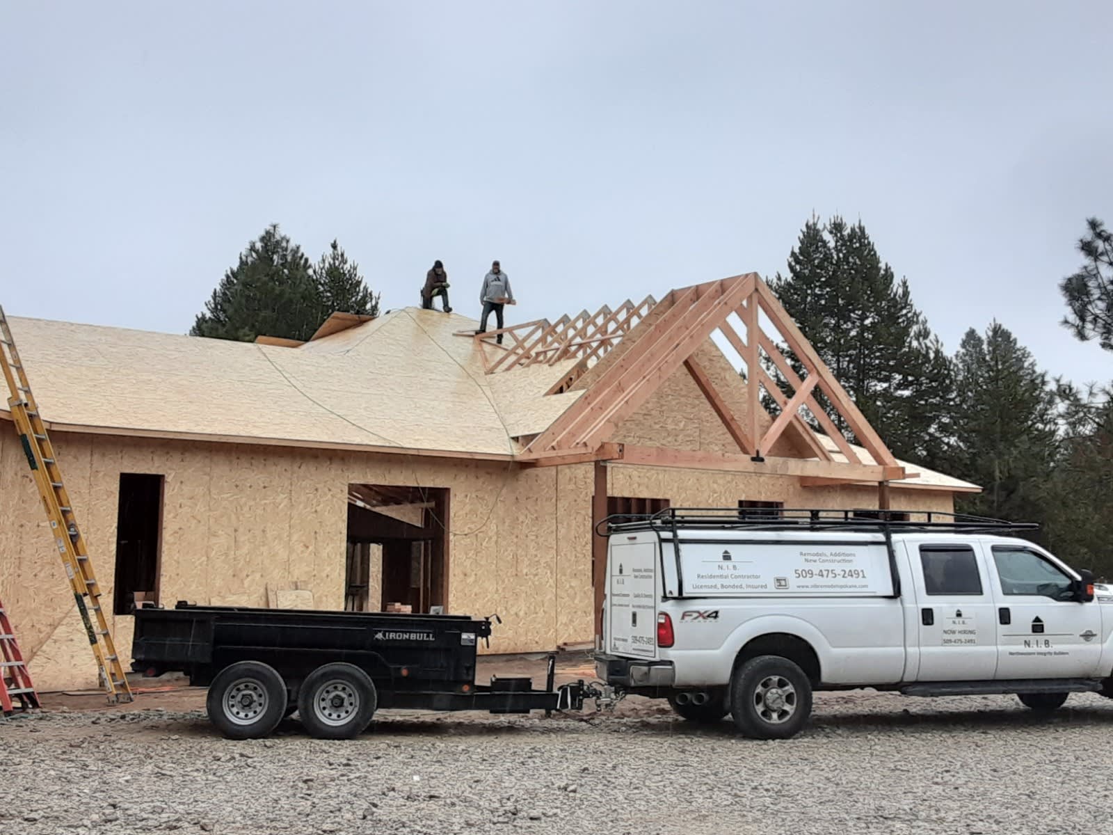 Two members of N.I.B. LLC standing on a roof of a house in-progress, finishing up a roof sheathing install