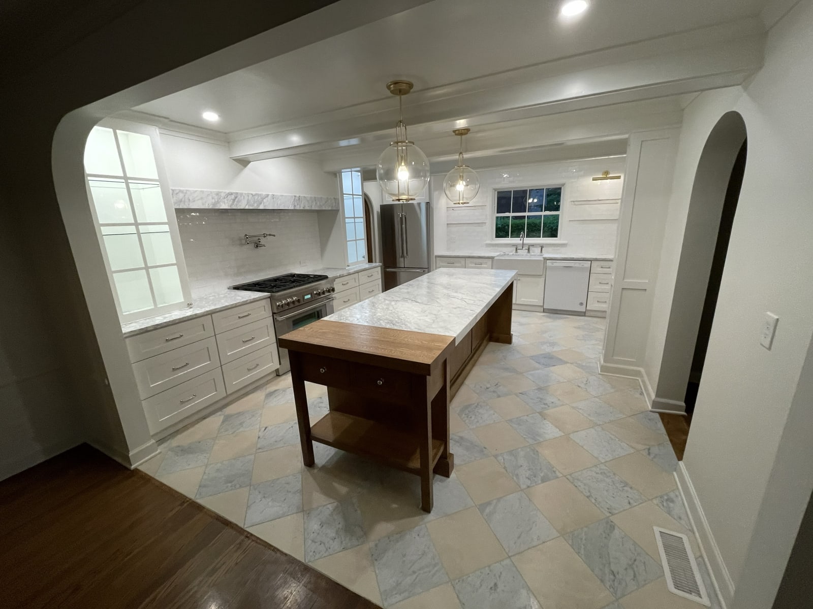 This kitchen remodel by NIB in Spokane, WA, perfectly combines timeless elegance with functional design. The white cabinetry with gold hardware complements the marble countertops, and the intricate marble tile flooring adds texture and contrast. The custom range hood and spacious island, with its warm wooden accents, serve as the kitchen's centerpiece. Thoughtful lighting fixtures illuminate the entire space, enhancing the refined and inviting atmosphere.