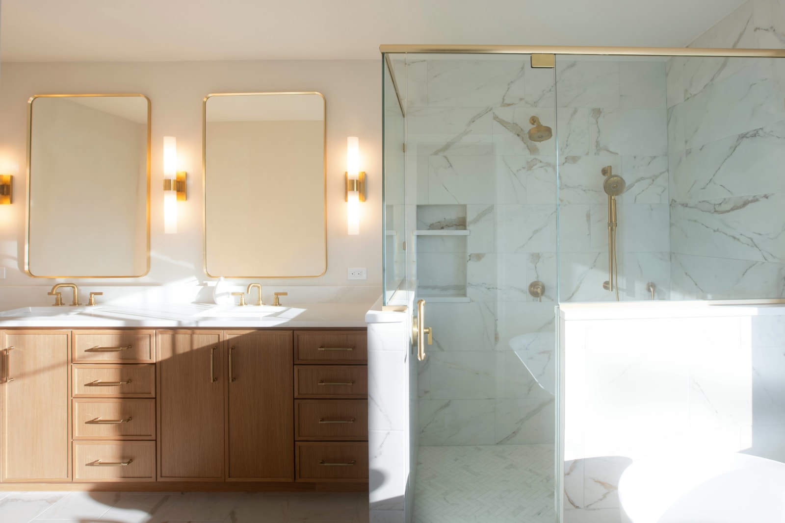 This elegant bathroom remodel was completed by NIB in the Spokane, WA area. The space features a luxurious combination of marble tiles and custom cabinetry. With golden fixtures and a spacious, frameless shower, the design brings both style and functionality to the room. Natural light floods the space, highlighting the soft finishes and modern fixtures, making it a serene and inviting retreat. The clean lines of the cabinetry and geometric pattern of the flooring complete the high-end look of this sophisticated bathroom.
