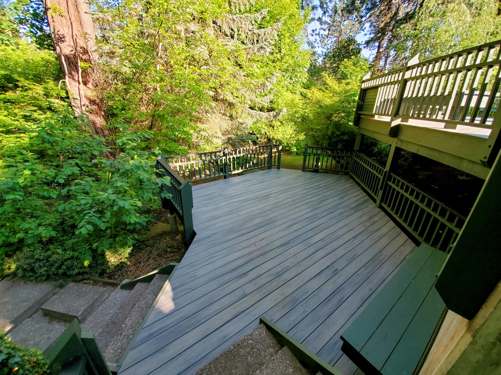 This tranquil outdoor space showcases a deck beautifully built by NIB in Spokane, WA. Nestled among greenery, the deck's clean lines and durable, long-lasting materials make it a perfect place to enjoy nature in comfort. The strategic design includes built-in seating and a staircase that connects to the lush landscape, offering a seamless blend of functionality and style, all crafted by NIB for a superior outdoor experience.