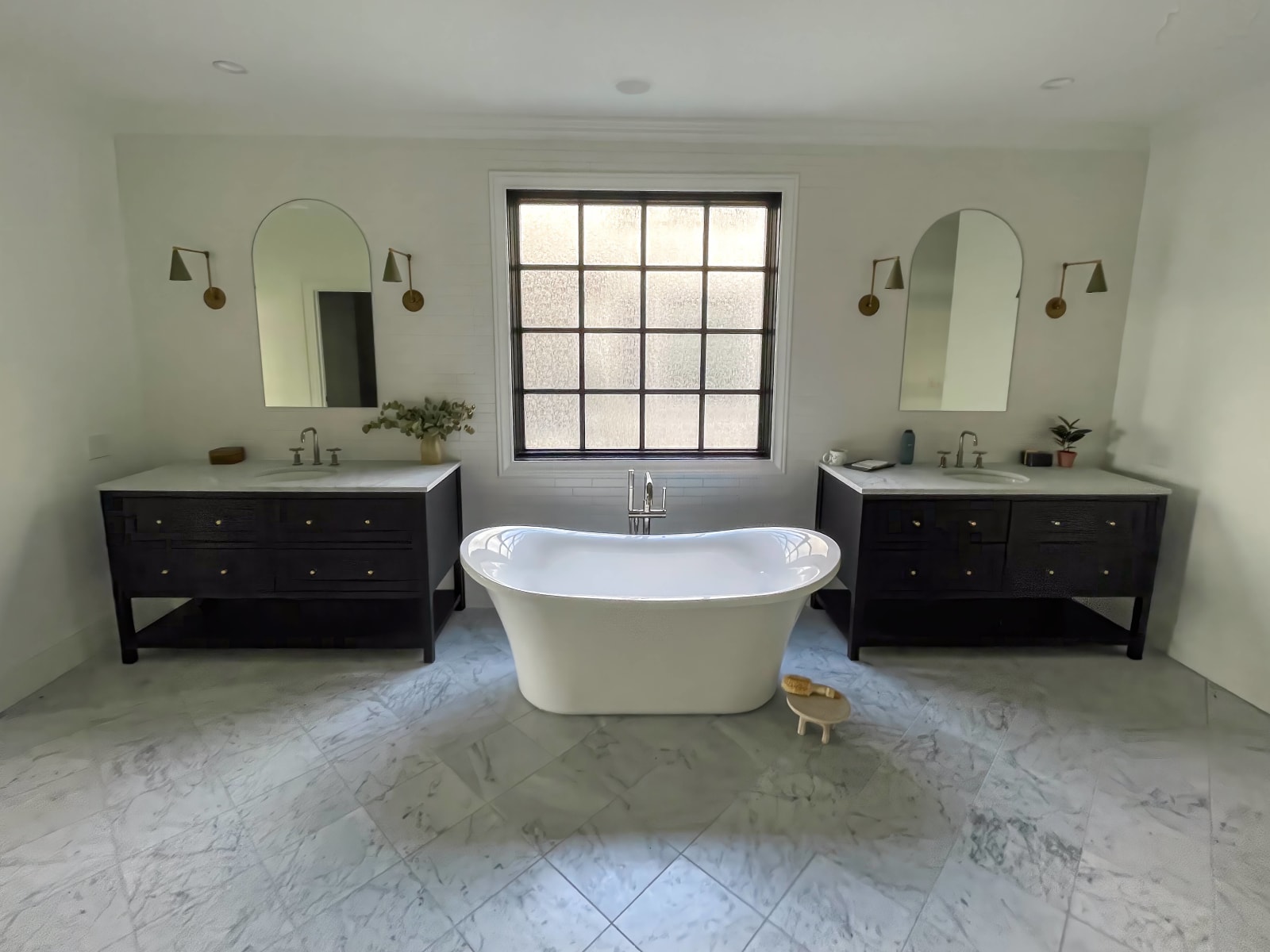 This bathroom remodel, completed by NIB in Spokane, WA, features elegant, modern finishes that create a serene, spa-like atmosphere. The freestanding bathtub is beautifully centered in the space, complemented by the two separate vanities with ample storage. The large window lets in natural light, creating an airy and inviting environment. The sleek black vanities paired with the marble flooring and clean lines throughout highlight the quality craftsmanship and attention to detail NIB brings to every project.