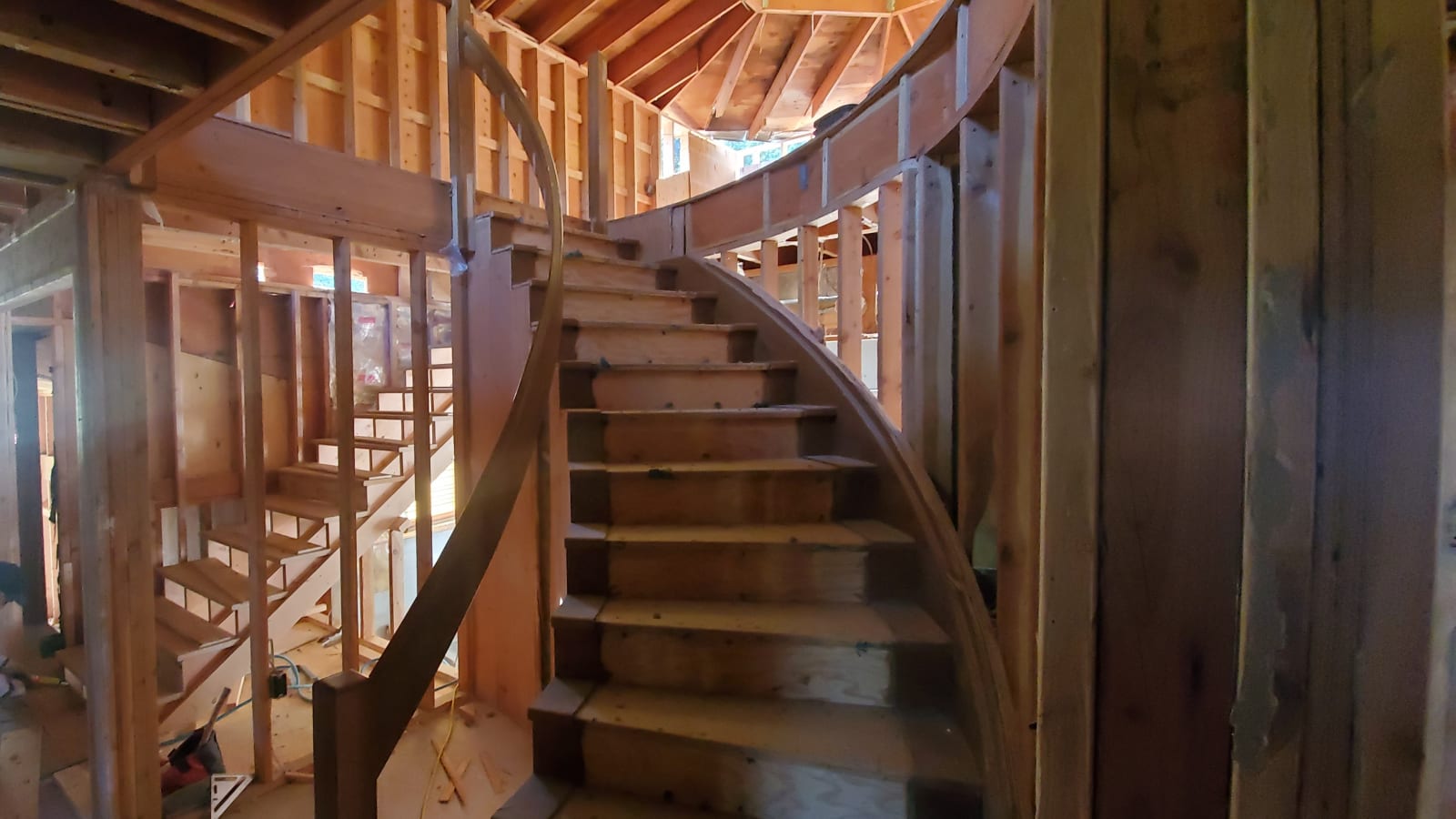 A stunning view of a curved staircase under construction by NIB around the Spokane Valley area of Spokane, WA. Showcasing delicate craftsmanship. The wooden steps and handrails are visible as they are being carefully built, with framing and unfinished walls surrounding the space. This image reflects NIB's attention to detail and expertise in creating intricate, custom features in home construction projects.