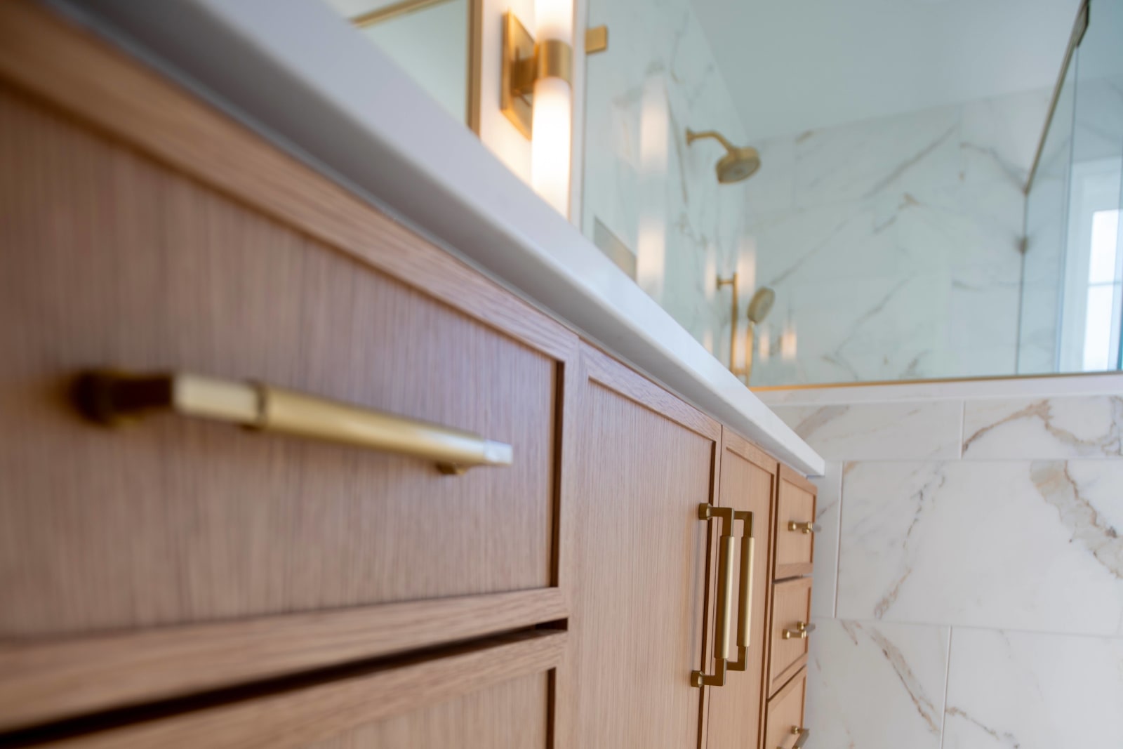 A close-up shot of a beautifully designed vanity from one of NIB's full bathroom remodel projects in Spokane, WA. The vanity features rich wood cabinetry with sleek gold hardware, including both drawer pulls and handles that add a touch of elegance. The marble countertop complements the clean, minimalist design of the space, with soft lighting casting a warm glow on the surfaces. This detail showcases the high-quality materials and craftsmanship NIB uses in their versatile product offerings, ensuring both style and functionality.