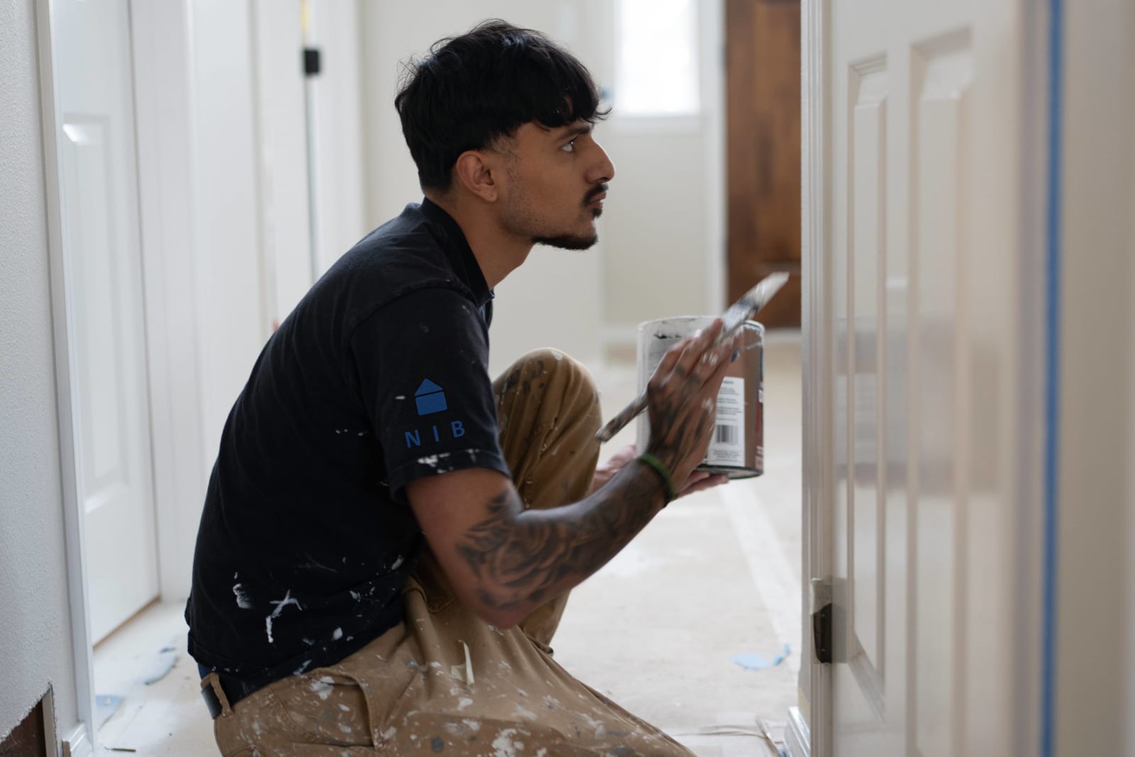 An NIB worker in the midst of applying final touches during an interior remodel in Spokane, WA, showcases the company's commitment to in-house workmanship. The worker, wearing an NIB-branded shirt, is carefully painting a door frame, with great attention to detail and precision. The clean, organized environment reflects NIB's high standards of quality and craftsmanship. The work area is still in progress, with the worker focused on delivering the best results, demonstrating the dedication NIB brings to every project.