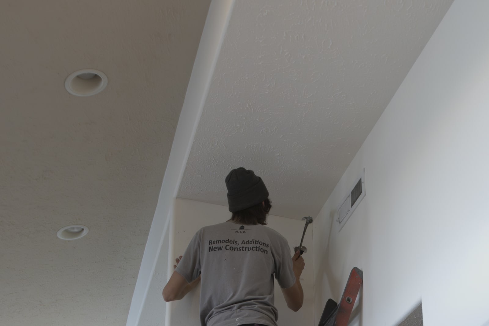 An NIB worker on-site during a project in Spokane, WA, demonstrating the company’s commitment to full-time project presence. The worker, dressed in an NIB-branded shirt, is using a hammer to finish a task on the ceiling, ensuring every detail is completed with care and precision. The clean, organized workspace and attention to the smallest tasks reflect NIB’s dedication to maintaining quality and efficiency throughout the entire process.