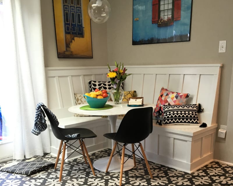 A cozy, newly designed seating and dining area done by NIB for a Spokane Metro WA home remodeling project with custom-built bench seating along the walls. The white wainscoting and patterned floor tiles create a clean, modern look, while bright, comfortable cushions in bold patterns add color and personality. A round dining table sits in the center, surrounded by light-filled windows.