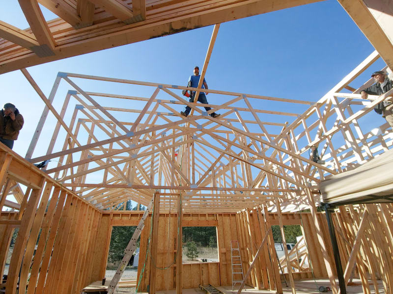 The NIB team is working on the trusses of a home, with the framework rising up under the clear blue sky. A few crew members are strategically positioned, carefully securing the structure while demonstrating the safety and teamwork that NIB is known for. The open space within the home’s frame highlights the scope of the project and the meticulous craftsmanship going into the construction.