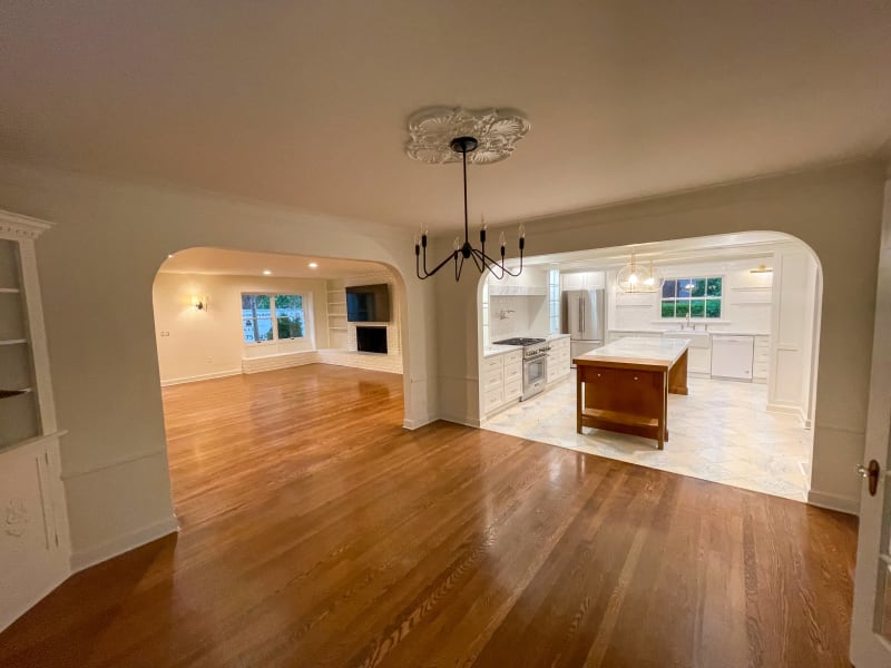 A spacious open-plan living area that has been beautifully remodeled by NIB in Spokane, WA. The elegant room features gleaming hardwood floors that seamlessly connect the living room and kitchen. The kitchen is a standout with its sleek cabinetry, white marble countertops, and a contrasting wooden kitchen island that adds a touch of warmth to the space. The archway between the living area and kitchen creates an inviting flow, perfect for both relaxing and entertaining.