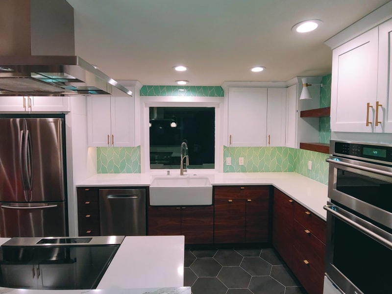 This beautiful kitchen remodel by NIB in Spokane, WA, showcases a vibrant and modern design with a bold use of color and materials. The bright green backsplash tiles bring a refreshing touch, complemented by the warm wood cabinetry and sleek white countertops. The inclusion of high-end appliances, such as a professional-grade range and farmhouse sink, enhances the functionality of the space. The hexagonal tile flooring and brass hardware add sophisticated accents, making this kitchen both stylish and practical for everyday use.