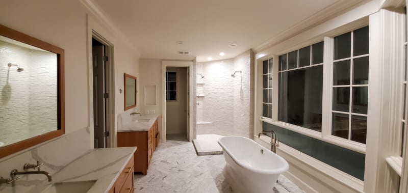This luxurious bathroom remodel, done by NIB in the Spokane, WA area, showcases sleek design and modern comfort. Featuring a freestanding tub and custom marble flooring, the space boasts both elegant finishes and high-end materials. The walk-in shower, surrounded by marble tiles with a herringbone pattern, creates a spa-like feel. Beautiful natural light pours in through the expansive window, offering stunning views while maintaining privacy. Every detail, from the custom cabinetry to the lighting fixtures, adds a touch of sophistication to this serene retreat.