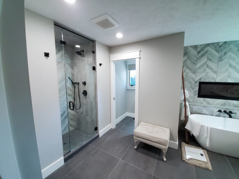 This beautifully remodeled bathroom by NIB in Spokane, WA, is a great example of how to create a spa-like retreat at home. Featuring sleek and modern design elements, the walk-in shower is framed with stylish black hardware and accented by striking chevron tile. The freestanding bathtub complements the contemporary aesthetic, while the large window lets in plenty of natural light. The balance of neutral tones and clean lines gives the space a calm, luxurious feel, perfect for relaxation.
