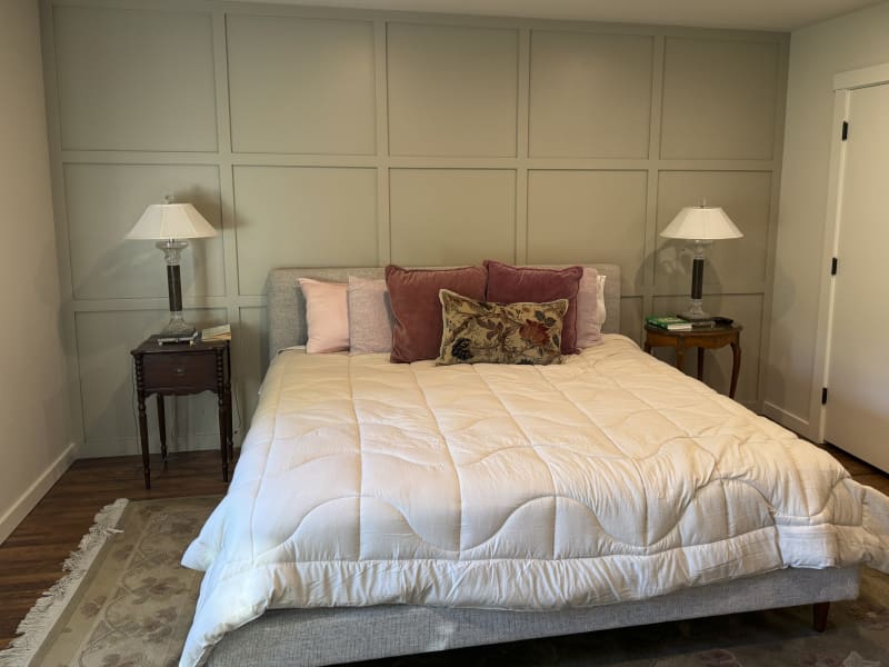 This inviting bedroom features custom paneling on the accent wall installed by NIB in Spokane, WA. The neutral tones of the paint and the luxurious textures of the bedding and pillows create a serene and restful atmosphere. The design, complemented by elegant nightstands and soft lighting, transforms the space into a comfortable retreat, balancing both style and function. The subtle details, like the clean lines of the paneling and the warm wood flooring, provide a perfect backdrop for relaxation.