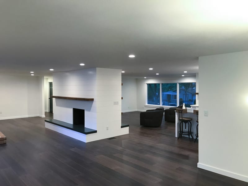 This beautiful open-concept living space, completed by NIB in Spokane, WA, showcases the perfect blend of modern style and functional design. The standout feature is the custom fireplace, with sleek white shiplap surrounding it and a contrasting rich wood mantle. The clean lines and minimalist design of the room are enhanced by the smooth, dark wood flooring and bright, airy windows that flood the space with natural light. The overall feel is welcoming and spacious, ideal for both relaxation and entertaining.