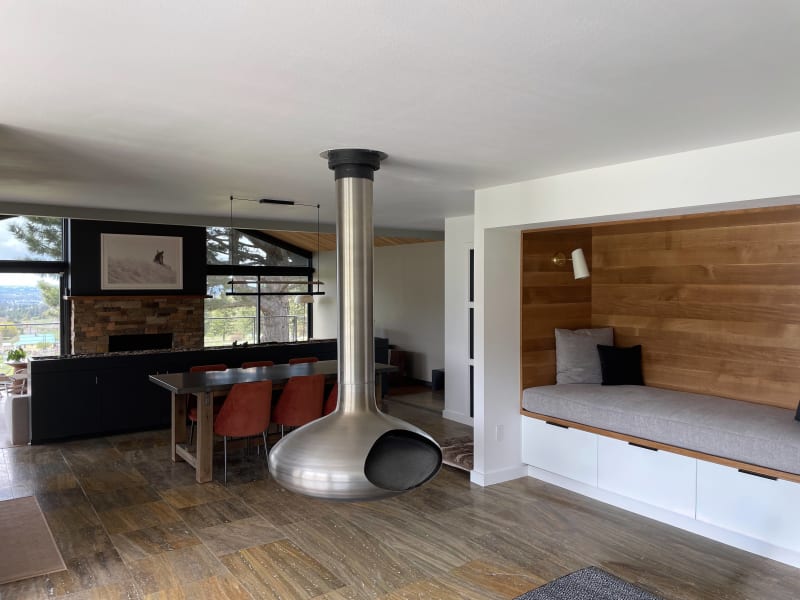 This stunning open-concept living space, remodeled by NIB in the Spokane, WA area, features a striking modern fireplace and a cozy reading nook. The sleek, suspended fireplace is a statement piece that draws the eye, while the rich wood elements and contemporary furnishings create a comfortable and inviting atmosphere. Large windows allow for plenty of natural light and offer expansive views, making this a perfect space for both relaxation and entertaining. The custom-designed bench seat adds a touch of warmth and functionality to this beautifully renovated room.