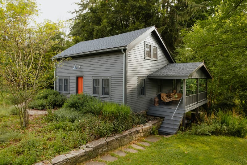 A beautiful siding installation. The home is framed with sleek, modern gray siding that complements the lush greenery surrounding it. The vibrant orange door provides a striking contrast against the muted tones of the house, adding a pop of color while still maintaining a balanced, harmonious look. 