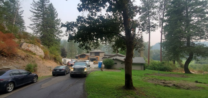 A construction site in the Spokane, WA area, done by NIB. A custom home is under construction. Partially completed home with visible framing, surrounded by vehicles and construction machinery. The site is nestled among tall trees, and the clear sky offers a glimpse of the surrounding landscape.