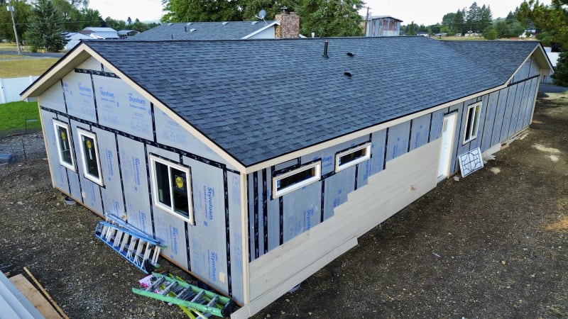 A custom home construction project in the Spokane, WA area, done by NIB. The building in its early stages. The roof is finished, and Styrofoam insulation is applied to the exterior walls, while the siding installation is still in progress.