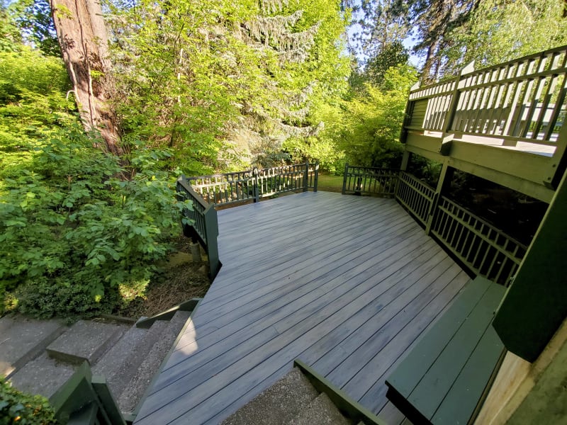 A large, multi-level deck in the backyard of a Spokane, WA home done by NIB. Featuring green railings and stairs leading to the lower yard. The deck is surrounded by lush trees and foliage, blending seamlessly with the natural surroundings.