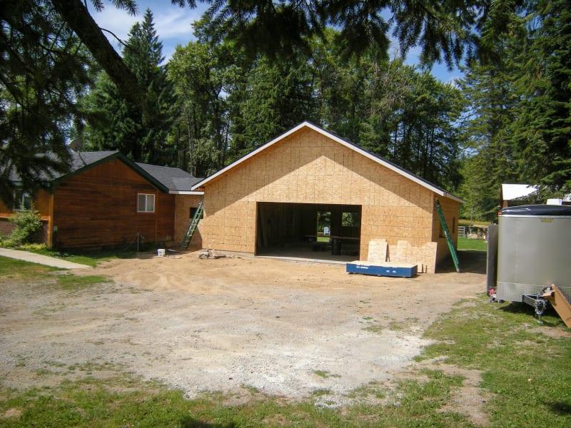 A home addition project by NIB in Spokane, WA, showing the framing stage of a new structure being added to an existing home. The walls are up, and the space is clearly taking shape with an open area for the garage or additional rooms. The site is clean and organized, with tools and materials neatly stored around the property. The addition is positioned for a natural integration with the current home, demonstrating NIB’s ability to expand living spaces while maintaining the aesthetic of the original structure.