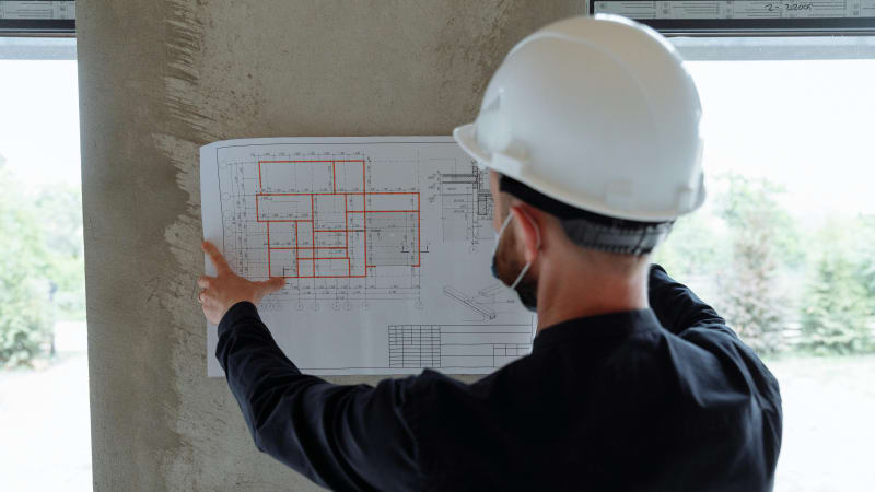 A construction professional carefully examines blueprints during the permitting and scheduling process for a custom home build. The detailed plans, marked with necessary adjustments and notes, guide the project through the approval process while coordinating timelines for each phase of the build. This image highlights the importance of thorough planning and communication in ensuring the successful completion of custom homes in Spokane, WA, with NIB managing the entire process from start to finish.