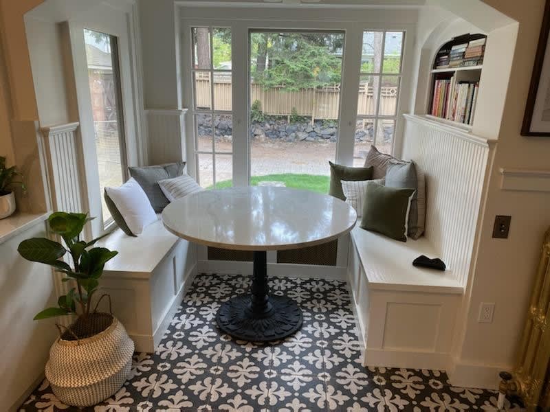 A cozy breakfast nook in a South Hill, WA, home, done by NIB. It features built-in seating with soft cushions and a round table. The large windows let in natural light, offering a comfortable space to enjoy meals or relax while taking in the views of the surrounding Spokane-area yard. The custom design fits seamlessly into the home's modern aesthetic.