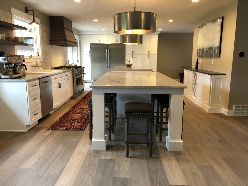 A beautifully remodeled kitchen in a home in the South Hill area of Spokane, WA, featuring modern white cabinetry, a spacious island with seating, and high-end stainless steel appliances. The sleek countertops and hardwood flooring complement the clean, contemporary aesthetic, while the statement pendant light fixtures add a touch of sophistication. 