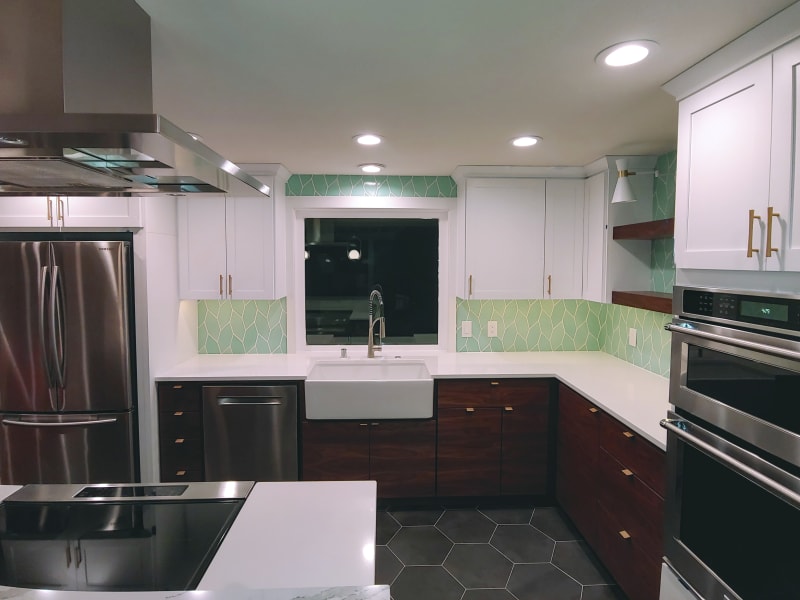 A beautifully designed living room fireplace in the Spokane Valley area of Spokane, WA. The fireplace features a striking herringbone-patterned tile surround in soft neutral tones, creating a sophisticated focal point. The white trim and mantle frame the fireplace, complementing the clean lines of the room. A modern gas fire glows gently inside, adding warmth and ambiance to the space. The surrounding hardwood flooring and cozy furniture complete the inviting atmosphere, making this a perfect living room centerpiece.