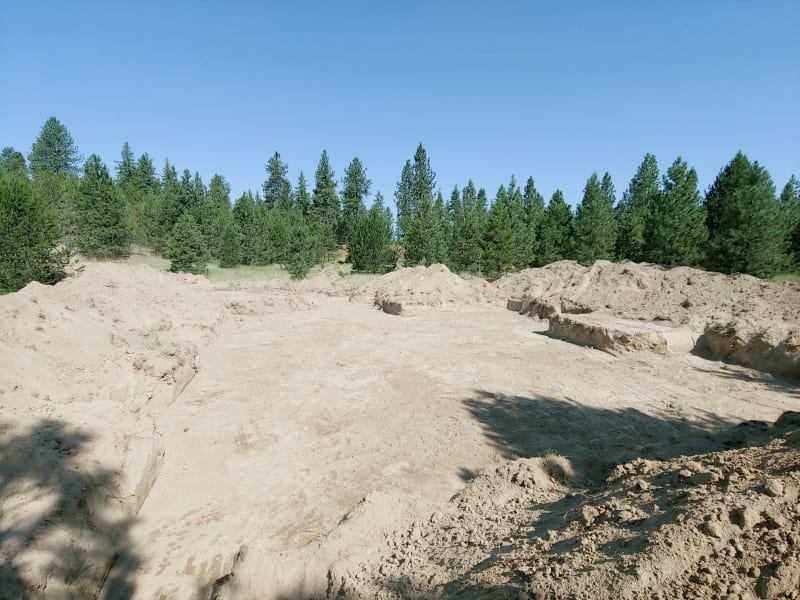 A cleared lot with the foundation trenching for a custom home under construction. The site is surrounded by dense trees, providing a secluded and scenic location for the build. This site preparation is a key step in NIB's custom home construction process, where careful excavation and planning are crucial for a solid foundation. The work is being completed by NIB, known for delivering quality and craftsmanship in Spokane, WA.
