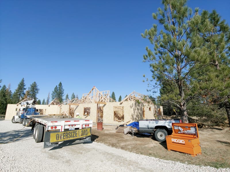 The exterior of a custom home under construction, with the framework and roof almost completed. The building is wrapped in Styrofoam insulation and partially covered with siding. The roof is shingled, and windows are in place but not yet fully sealed. The construction site is neat, with ladders positioned against the wall and some construction materials stored nearby. This project is being developed by NIB in Spokane, WA, showcasing the company's expertise in custom home building.