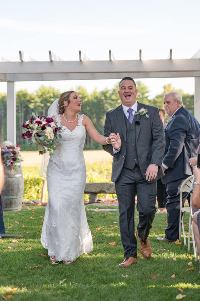 Bride and groom walking with a burgundy and white bridal bouquet by Designs By Don Florist.
