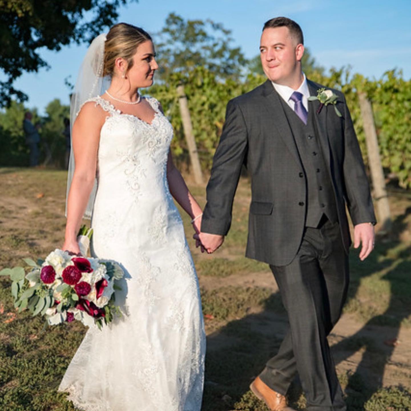 Bride and groom walking outdoors with a burgundy and white bridal bouquet for a New England wedding.