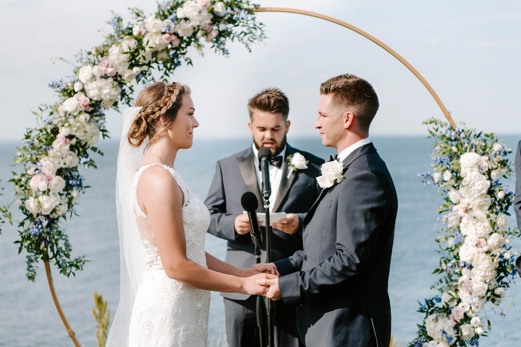 Oceanfront wedding ceremony with a floral arch designed with white, blush, blue, and greenery flowers.