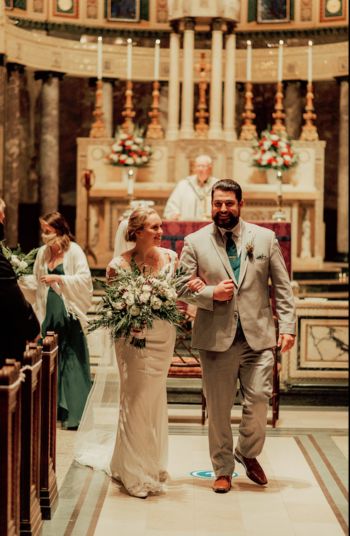 Bride and groom in a church with a lush greenery bridal bouquet and wedding boutonniere.