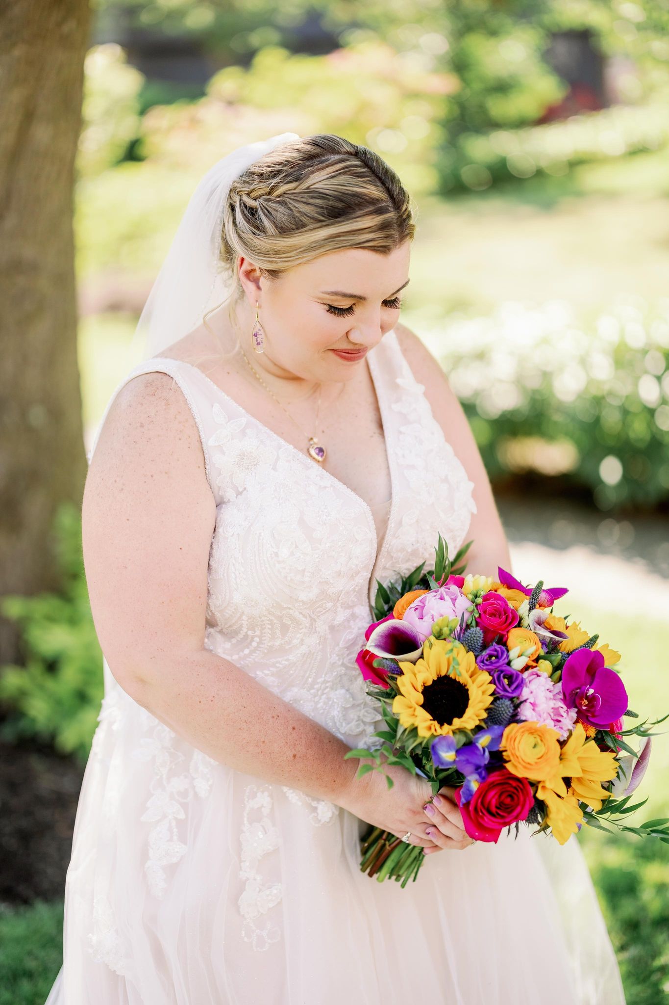 Bride holding a colorful wedding bouquet with sunflowers, orchids, roses, and bright seasonal flowers.