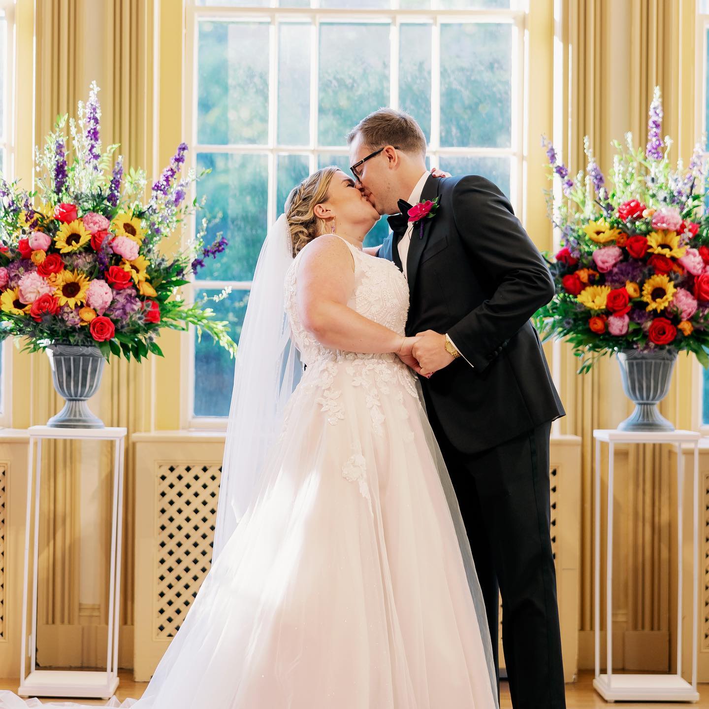 Bride and groom with colorful ceremony flowers featuring sunflowers, roses, purple blooms, and greenery.