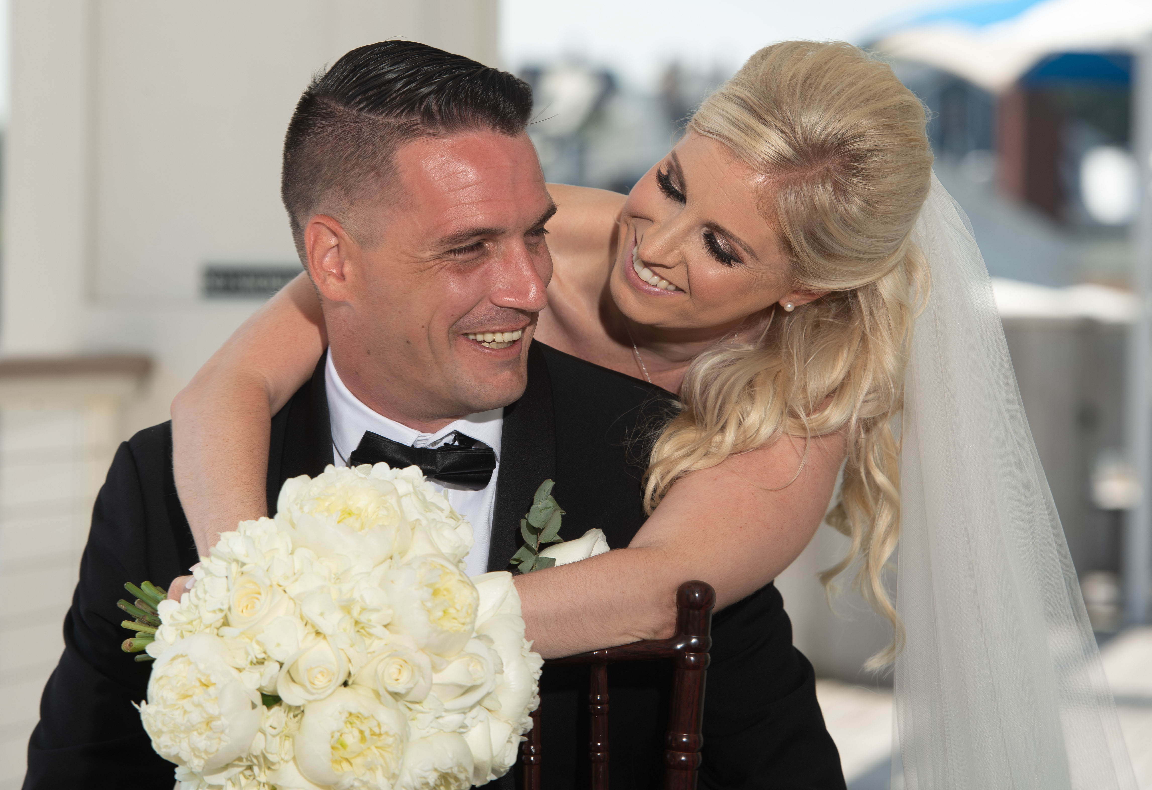 Bride and groom smiling with a classic white bridal bouquet by Designs By Don Florist.