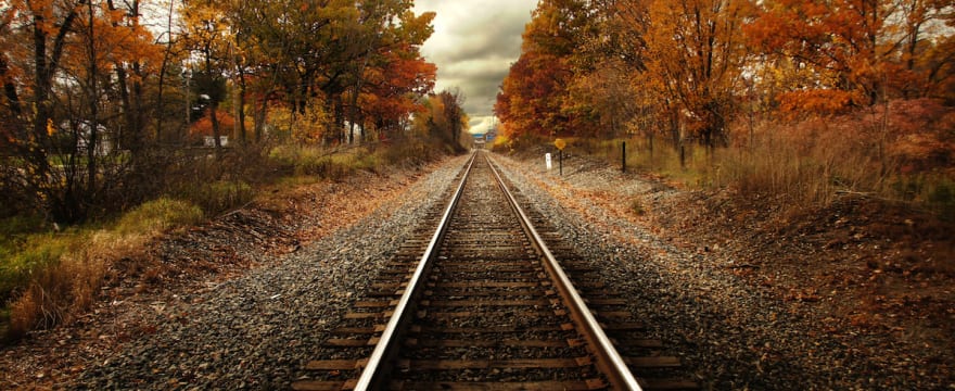 Empty road or railway tracks converging toward a vanishing point on the horizon, demonstrating leading lines