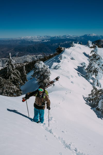 Un skieur porte ses skis en montant une arrête pour descendre une voie en hors-piste