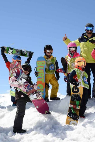 Un groupe d'enfant avec un moniteur en cours de snowboard