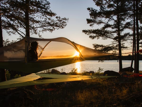 Une personne assis dans une tente hamac dans la forêt au coucher de soleil