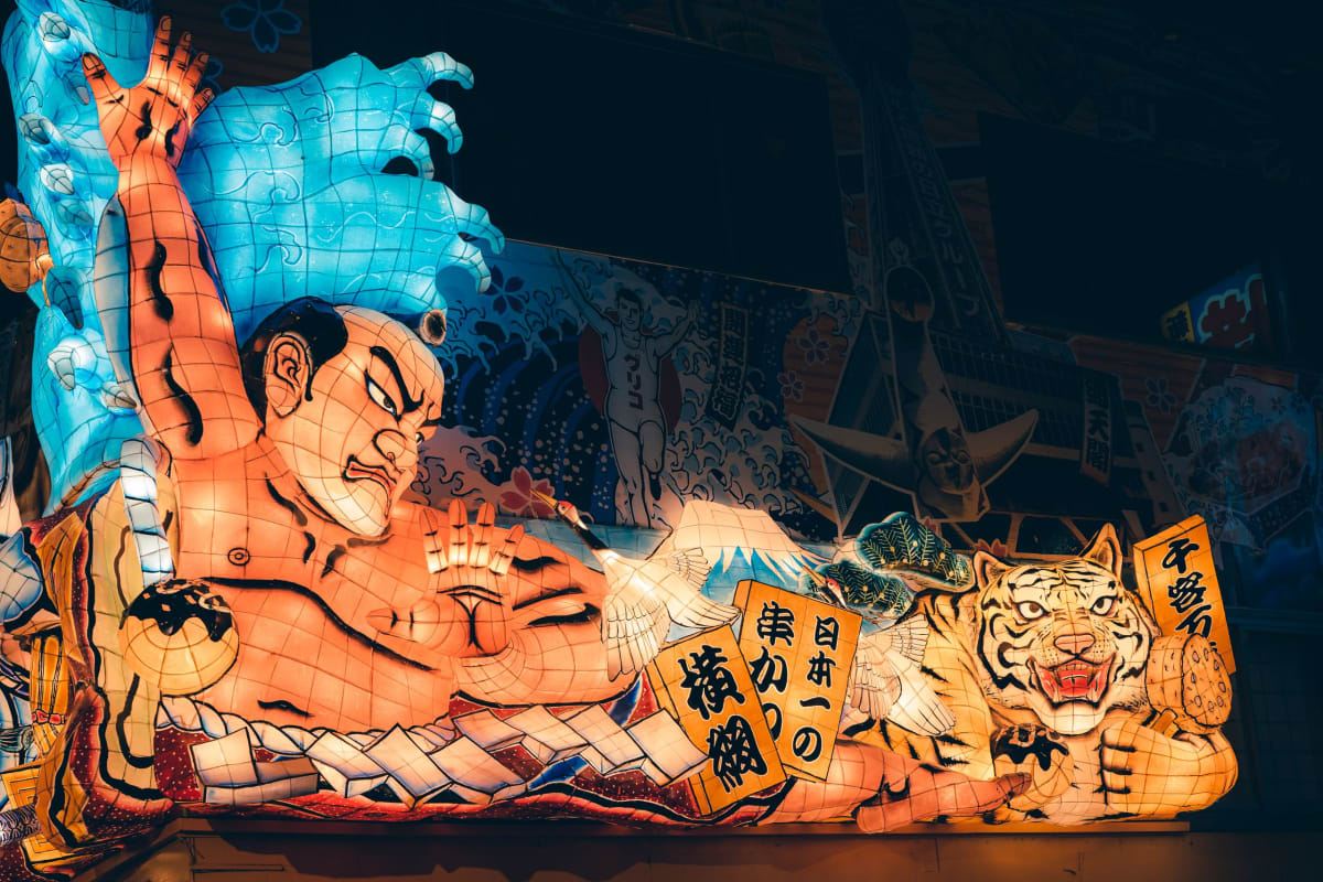 A huge illuminated paper-and-wire Nebuta float glowing in the dark, paraded through Aomori's streets surrounded by dancers
