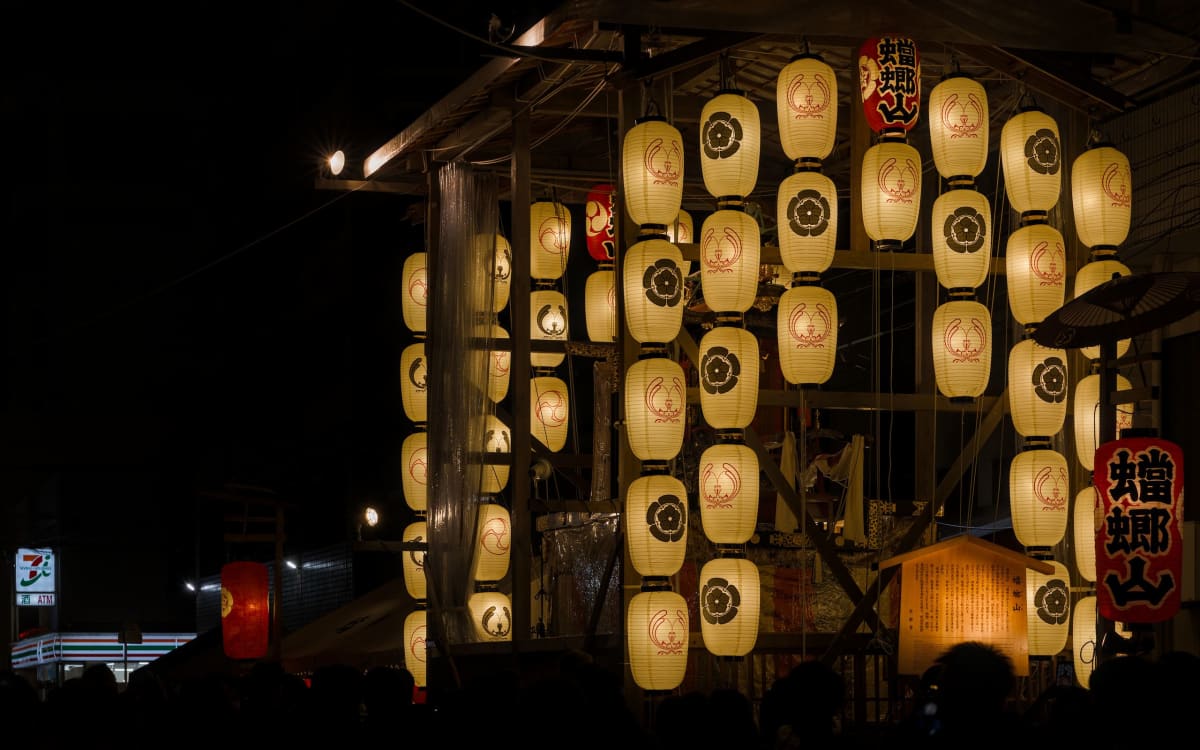 Paper lanterns lighting a tall Gion Matsuri yamaboko float on a pedestrianized Kyoto street at night