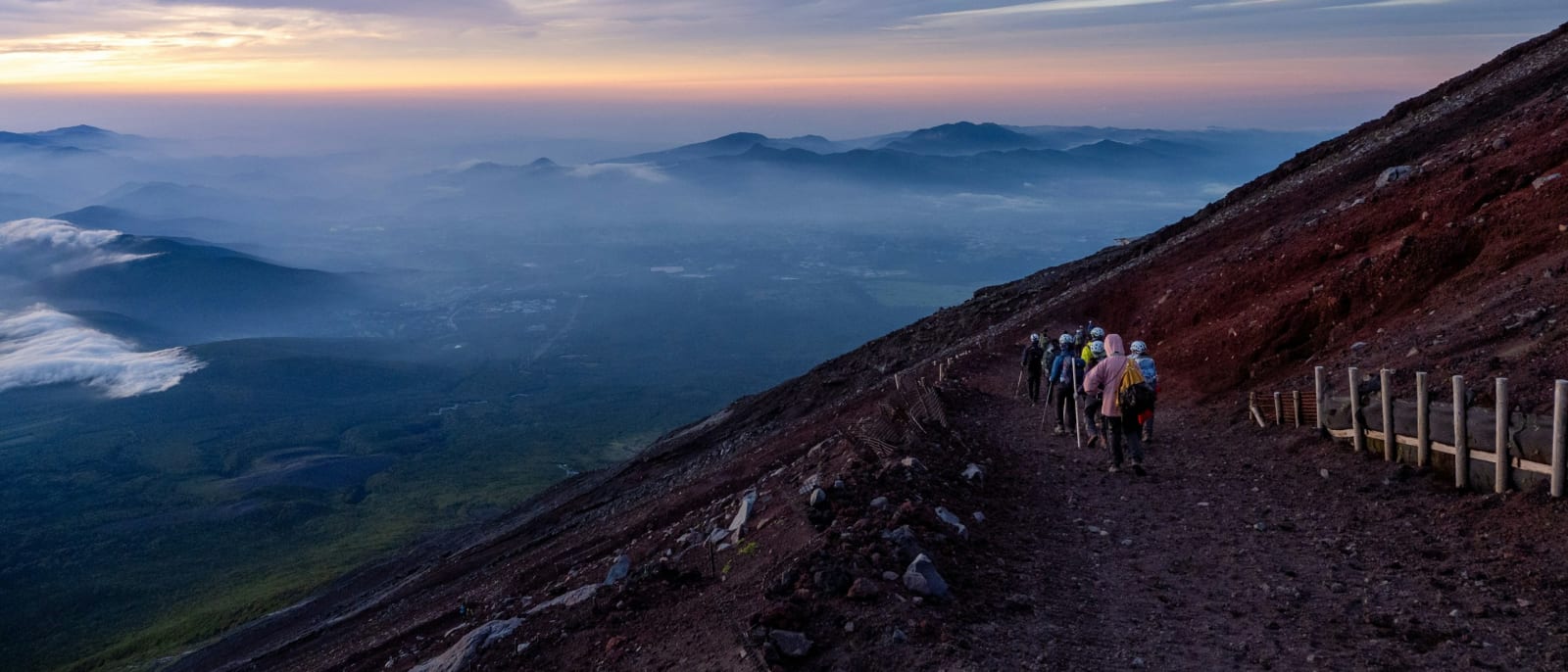 Climbers on the red scree of Mt Fuji's Yoshida Trail at dawn, with the plain far below