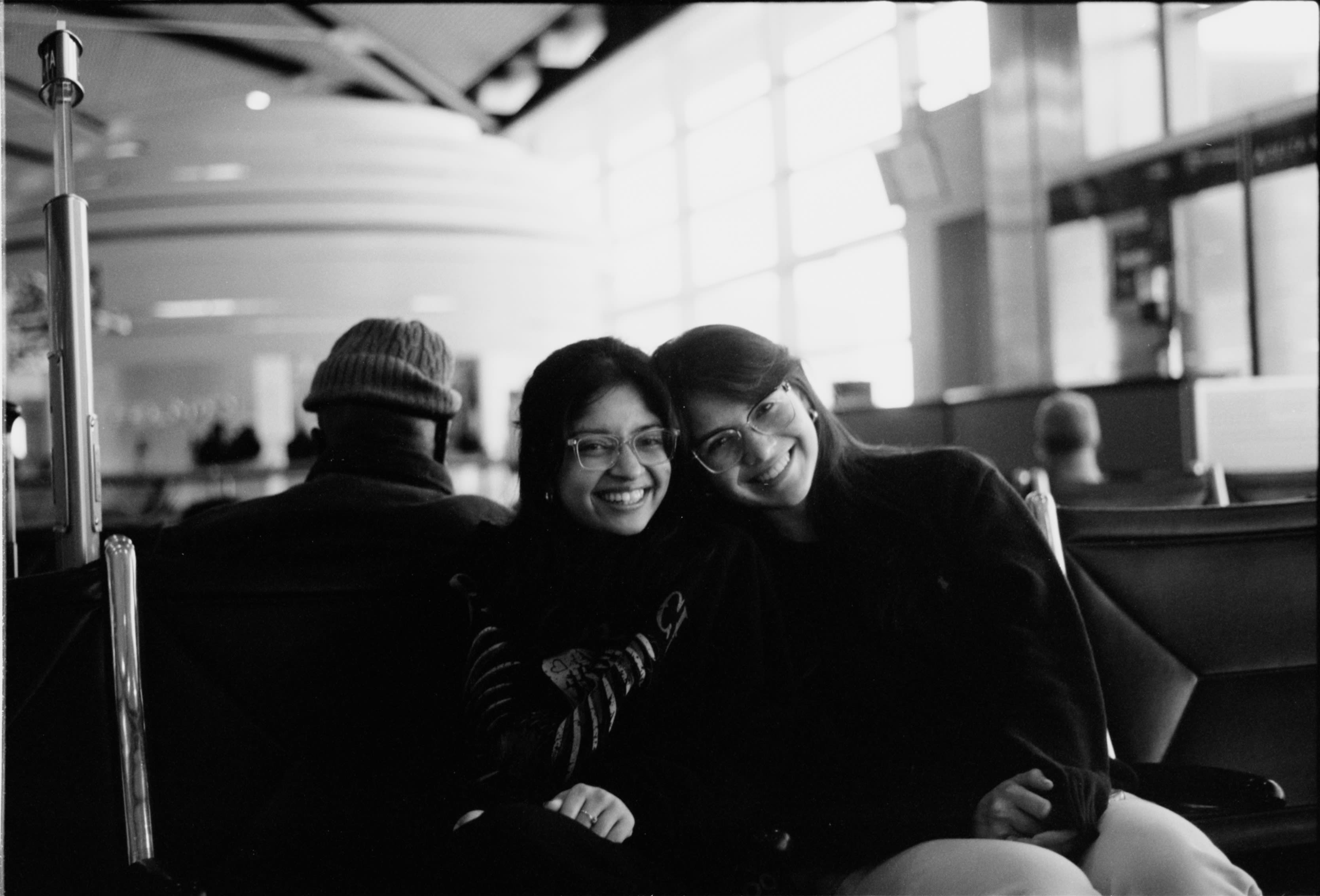 Two friends leaning into each other at an airport gate