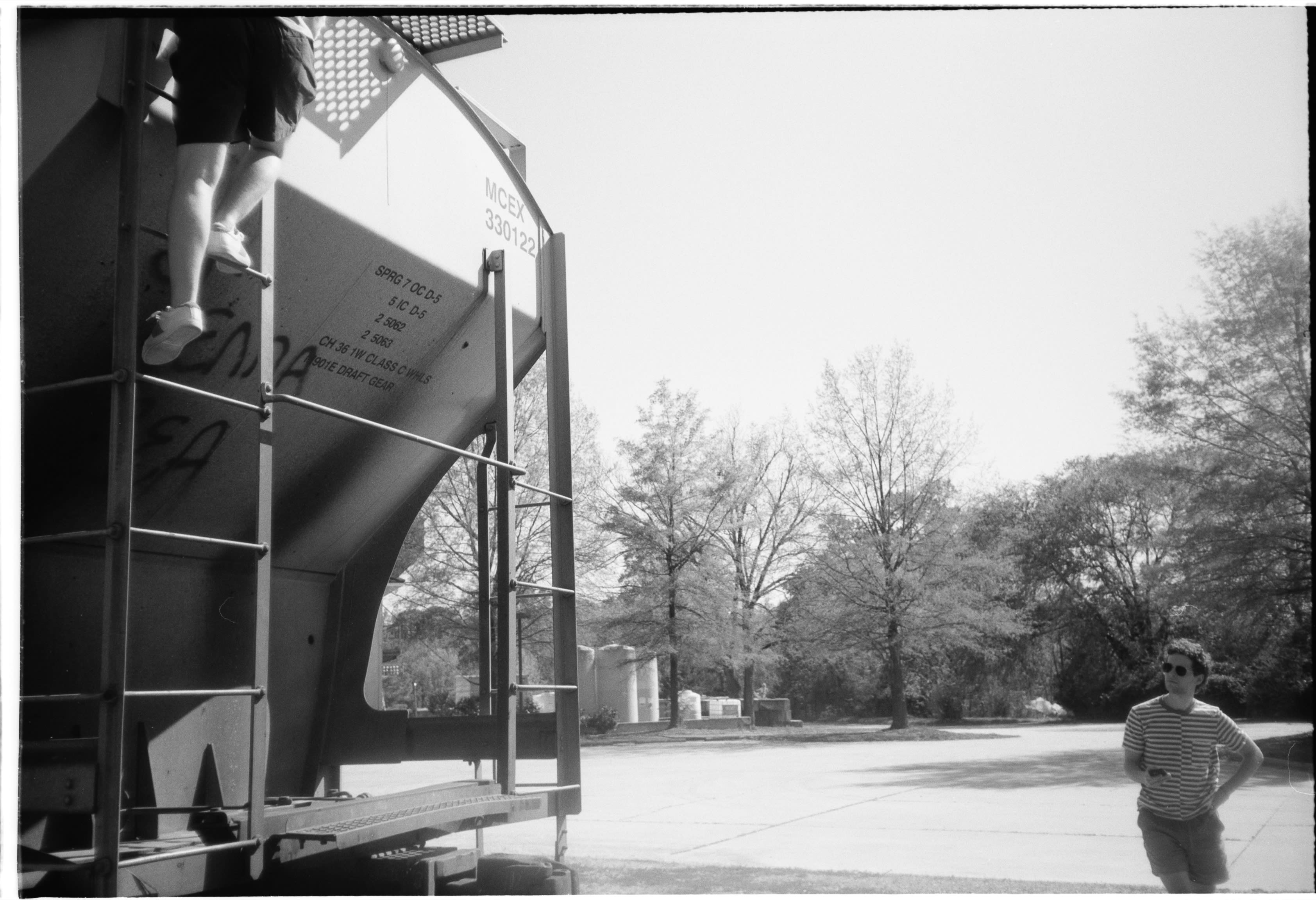 Someone on the rail car's ladder while a friend in a striped shirt walks over