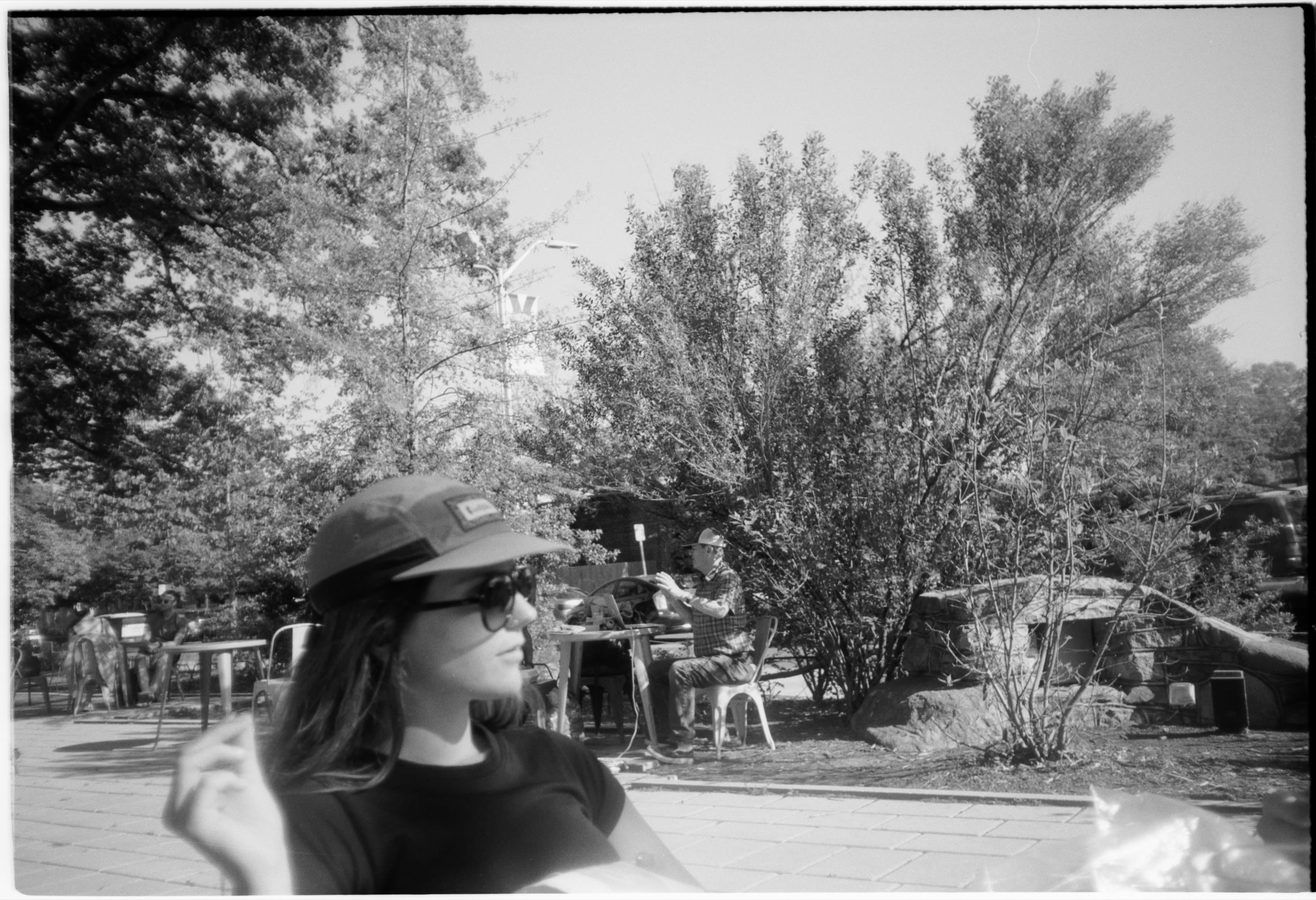 A friend in a cap and sunglasses outside, with people at tables behind