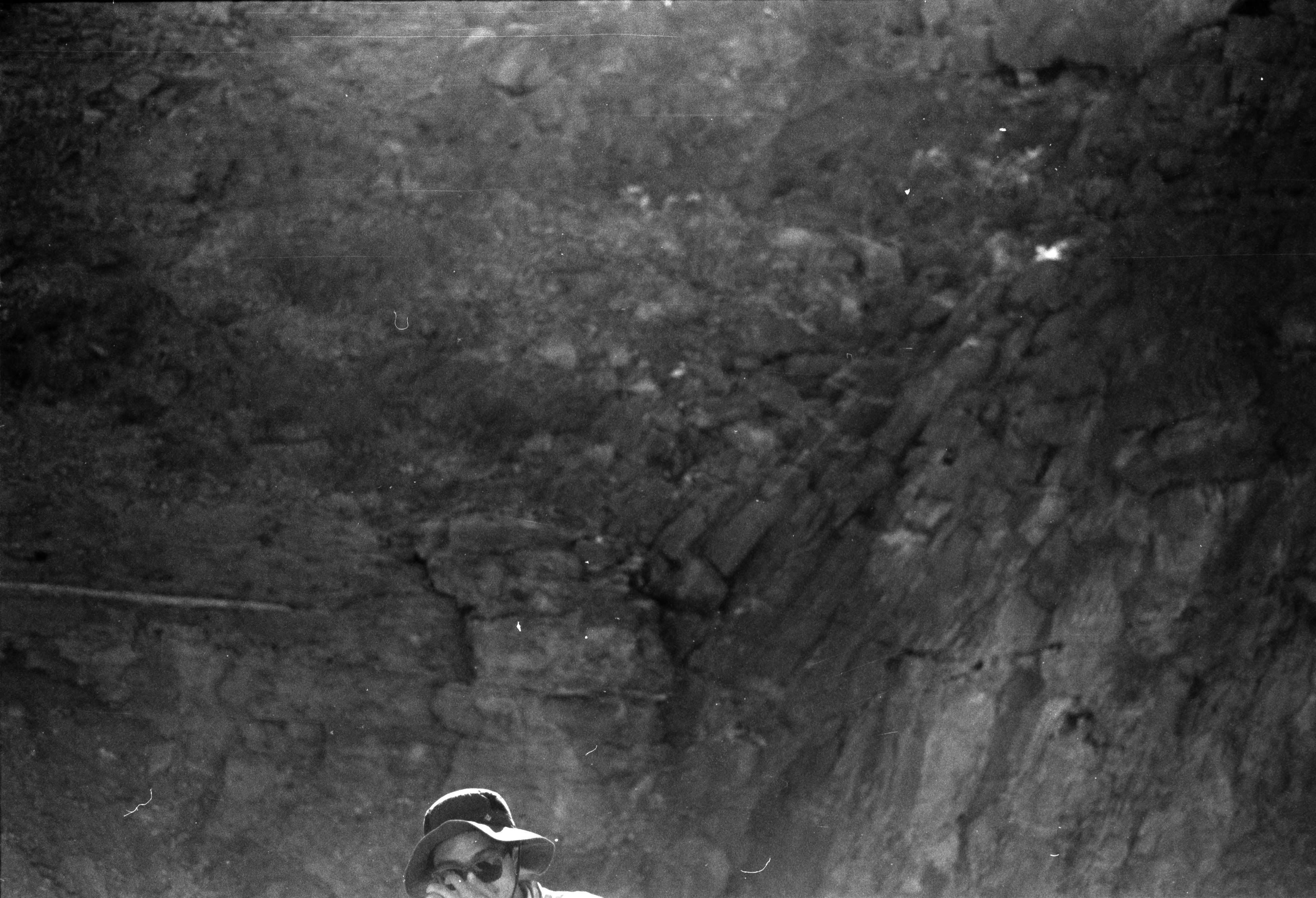 A hiker in a hat at the foot of a steep rock wall