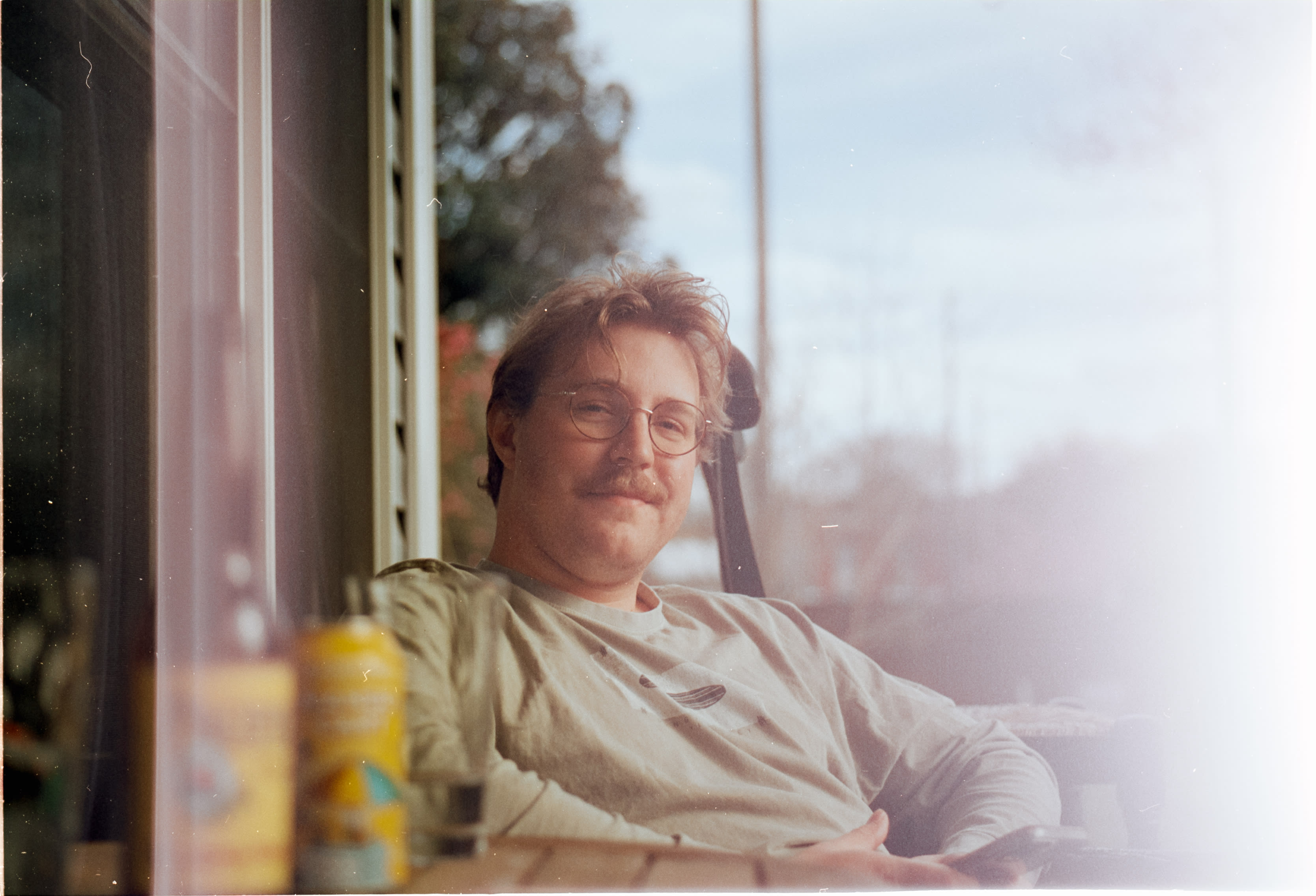 A friend with glasses and a mustache leaning back by a sunlit window